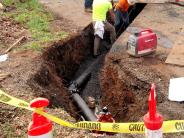 Contractors in construction ditch with caution tape and cones. 