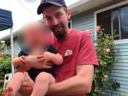 Terry Shinaver in red shirt and baseball cap holding a child