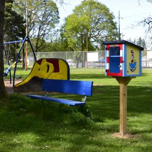 Cat in the Hat painted Little Free Library on post in park with playground equipment in background 