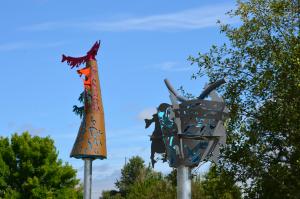 Two metal sculptures with trees and salmon next to each other with sky and trees in the background. 