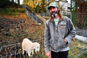 Mayor Rick Scholl stands next to goat behind fence on waterfront property. 