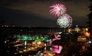 Two fireworks light up the night sky and reflect off the Columbia River with St. Helens waterfront buildings lit 