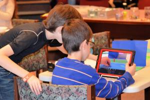 Two kids using iPad to take screenshot of small set they have created for stop motion animation project.