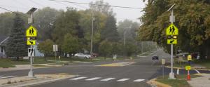Example of two rapid flashing beacon signs installed at edges of sidewalk between crosswalk 
