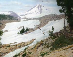 Glass Lantern Slide colored image of Mount Hood with historical hikers crossing a snow field in foreground 