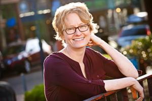Headshot of author Amy Stewart smiling, leaning arms against metal railing outdoors. 