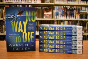 Upright hardcopy of "No Way to Die" book next to stack of paperback versions 