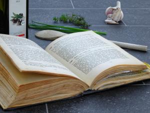 Cook book open on counter with cooking utensil and food around