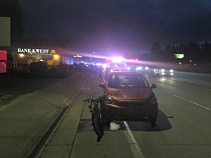 Vehicle crash on road with bicycle and emergency service lights in background 