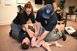 Two people kneeling over person laying on ground practicing first aid on a shoulder. 