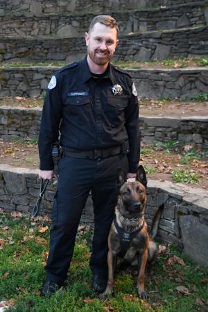 St. Helens Officer Bryan Cutright stands next to police canine Jax with stone amphitheater steps in the background