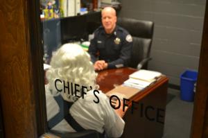 Office door closed with Cheif's Office written across window and police chief and man sitting at desk visible through window.