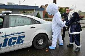 Person in Abominable Snowman outfit being handcuffed by Officer Claus and police officer in front of patrol car. 